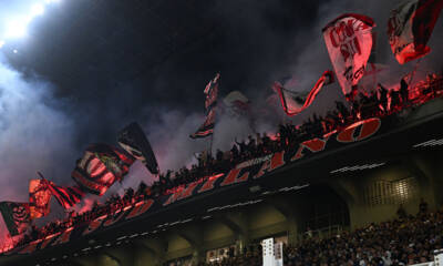 La Curva Sud di Milano al secondo anello blu di San Siro, con bandiere e striscioni, mentre i tifosi sostengono la squadra durante un’importante partita.