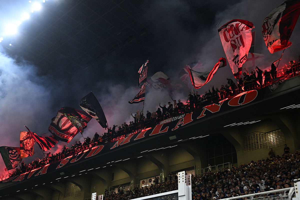 La Curva Sud di Milano al secondo anello blu di San Siro, con bandiere e striscioni, mentre i tifosi sostengono la squadra durante un’importante partita.