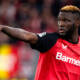 Victor Boniface con la maglia del Bayer Leverkusen indica una direzione ai compagni di squadra con il braccio